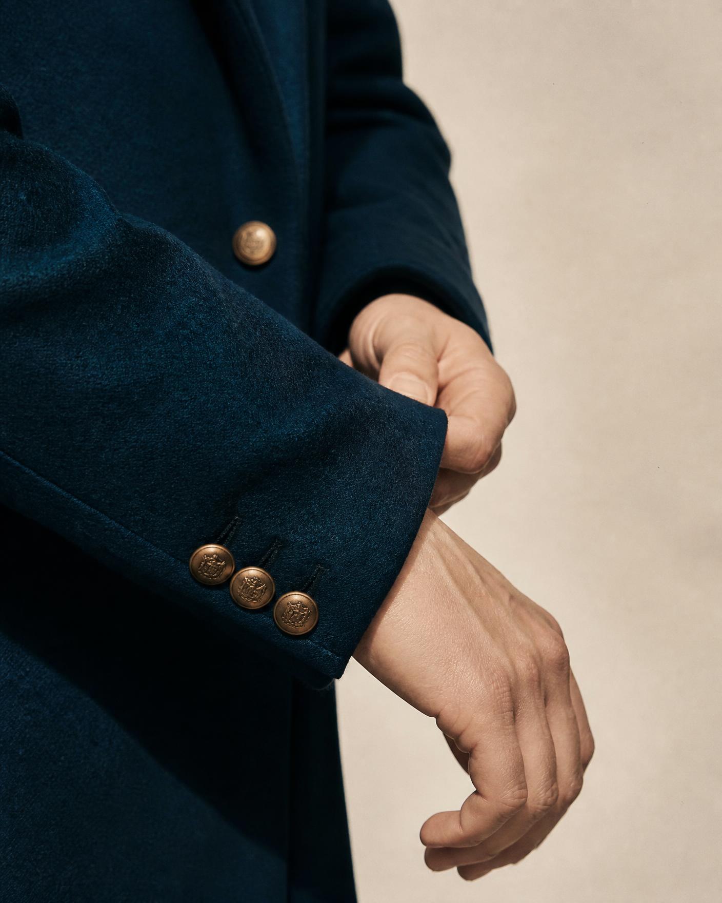 Détail d'une veste en laine bleu pétrole, poignet ajusté et boutons bronze